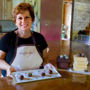 Diane Haase, owner of Truffle Me! displaying homemade chocolate truffles on a dessert tray with blocks of white and milk chocolate