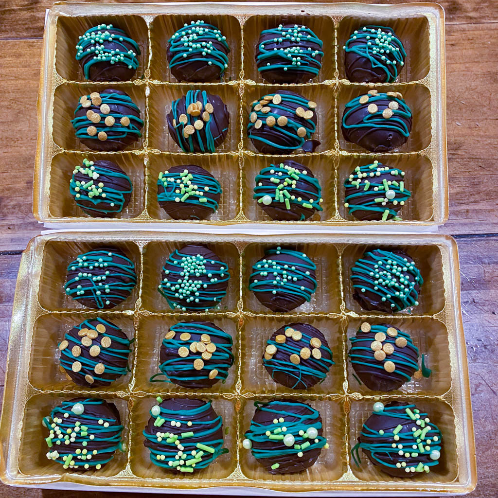 Chocolate Truffles decorated with green chocolate swirls and green sprinkles on top inside of a display case for Saint Patricks Day